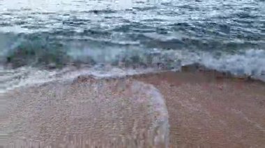 Sakin bir okyanus dalgası, sahil doğasının güzelliğini gösteren kumlu bir kumsalla nazikçe karşılaşır. Huzur ve rahatlama, dinginlik, seyahat ve doğal manzara temaları için mükemmeldir..