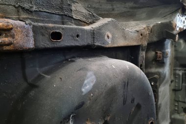 Paslı bir aracın, eski metal ve aşınmayı gösteren yakın çekim görüntüsü. Doku ve renkler, zaman ve elementlerin otomotiv bileşenleri üzerindeki etkisini vurgular, restorasyon ve onarım kavramları için idealdir.