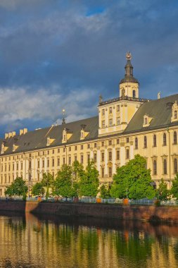 Wroclaw, Polonya, 15 Mayıs 2025: Büyük tarihi bir üniversite binası nehir kenarında, sıcak günbatımı renkleriyle yıkanmış olarak görkemli bir şekilde duruyor. Mimari ayrıntılar, tarihsel geçmişi ve akademik mirasını yansıtan altın ışıkla vurgulanır..