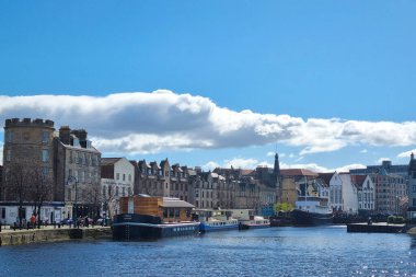 Edinburgh, İskoçya, 30 Mart 2025: Edinburgh 'un tarihi rıhtım manzarası, çeşitli mimari stiller sergileniyor. Sakin su, berrak mavi gökyüzünün altındaki canlı binaları yansıtır. Tarihle doğanın mükemmel bir karışımını sunar.