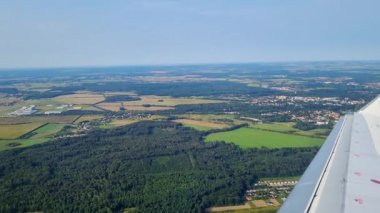 Wroclaw, Polonya, 28 Haziran 2024: Geniş hava manzarası yemyeşil tarlalar, ormanlar ve kasabaların bir kısmını gösteriyor. Uçak kanadı seyahat ve keşif öneriyor, kırsal kesimin doğal güzelliğini ve enginliğini yukarıdan yakalıyor..