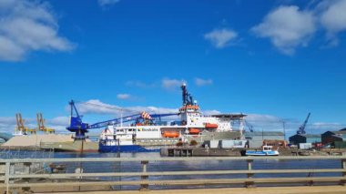 Edinburgh, İskoçya, 30 Mart 2025: Kargo gemileri ve endüstriyel ekipmanlar açık mavi gökyüzüne karşı hareketli bir limanı işgal ediyor. Turnalar malları boşaltıyor, modern bir liman ortamında denizcilik ticaret ve taşımacılığın dinamik atmosferini sergiliyor.