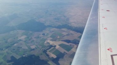 Bir uçak penceresinden görüldüğü gibi çeşitli tarımsal manzaranın hava perspektifi. Sahne, açık gün ışığı, kırsal arazi desenleri ve dokuları altında çeşitli yeşil ve kahverengi tonlarında geometrik alanlar sergiliyor..
