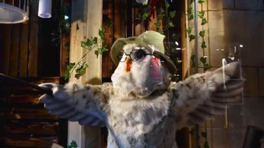 Londra, İngiltere, 17 Ocak 2025: Ahşap dokular ve tırmanma sarmaşıklarının zeminine kurulmuş, pelüş bir baykuşun şapka ve gözlük taktığı tuhaf bir ekran. Baykuşların kanatları genişçe açılır ve büyülü ve eğlenceli bir atmosfer yaratır..