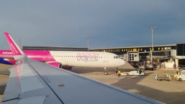 Barselona, İspanya, 4 Ocak 2025: Uçak, yer ekibi ve ekipmanlarıyla birlikte modern bir havaalanı terminaline park edilmiştir. Gün ışığında çekilen sahne, havanın hareketli atmosferini gösteren başka bir uçağın kanadını da içeriyor.