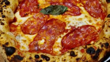 Eriyen peynir, sulu pepperoni dilimleri ve taze fesleğen yaprağı içeren taze pişmiş pepperonili pizzanın yakın çekimi. Altın, kıtır kıtır kıtır, dokuma katıyor, böylece yemek promosyonları ve restoran menüleri için ideal hale geliyor..