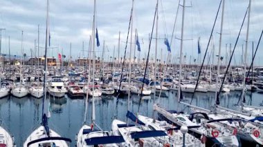 Barselona, İspanya, 3 Ocak 2025: Yelkenliler ve yatlar, uzun direkler ve yumuşak bulutlu gökyüzü tarafından çerçevelenmiş yoğun bir marinaya demirlemiştir. Huzurlu liman sahnesinde deniz teması ve sakin deniz manzaraları sergileniyor. Seyahat, eğlence ve deniz manzarası için ideal.