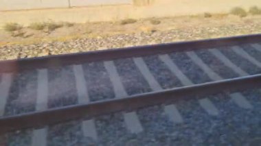 Demiryolu rayları çakıl döşeğinde paralel gidiyor ve verimli ulaşım için gerekli altyapıyı sergiliyor. Güneş ışığı, demiryolunun sağlam yapısını ve doğrusal perspektifini vurgulayan ince gölgeler bırakıyor..