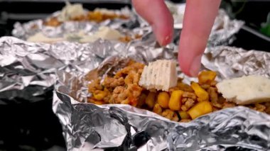 Mısır ve peynirle karıştırılmış, kamp yapmak ya da barbekü yapmak gibi açık hava aktiviteleri için idealdir. Bir el, folyoya sarılmış malzemelerin üzerine peynir dilimi yerleştirirken görülüyor..