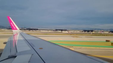 Barselona, İspanya, 24 Aralık 2024: Uluslararası bir havaalanından havalanmaya hazırlanan uçak kanadını gösteren bir uçağın manzarası. Uzak uçbirim ve bulutlu gökyüzü dinamik bir yolculuk atmosferi yaratır..