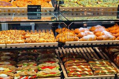 Viyana, Avusturya, 5 Mayıs 2025: Bir fırın vitrininde pizza dilimleri, hamur işleri, kruvasanlar ve sandviçler de dahil olmak üzere çeşitli yeni pişirilmiş ürünler sergilenmektedir. Her parça ahşap tepsilerde düzgün bir şekilde düzenlenir, müşterileri hem yemek hem de yemek seçenekleri ile baştan çıkarır.