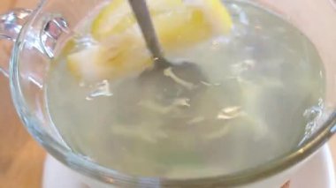 Şeffaf cam bardakta ferahlatıcı bir limon çayının yakından görüntüsü, limon dilimleri ve karıştırıcı bir kaşıkla. Gıda fotoğrafçılığında sağlıklı içecek kavramlarının tanıtımı için ideal..