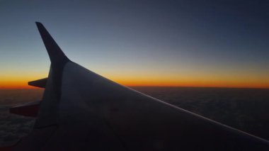 Barselona, İspanya, 24 Aralık 2024: Canlı bir günbatımı gökyüzüne karşı siluet oluşturan uçak kanadı, bulut katmanının üzerinde turuncu ve mavi renklerin çarpıcı bir karışımını sergiliyor. Seyahat, keşif, havacılık ve yolculuk teması için ideal..