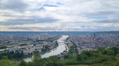 Rouen, Fransa, 29 Temmuz 2025: Rouen 'in dolambaçlı nehir, tarihi mimari ve engin şehir manzarasını dramatik, bulutlu bir gökyüzü altında gösteren panoramik manzara. Kentsel ve doğal elementlerin karışımı cazibeyi ortaya çıkarır..