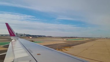 Barselona, İspanya, 24 Aralık 2024: Havaalanı pistindeki uçak taksileri olarak kanadı gösteren bir uçak penceresinden bakın. açık gökyüzü ve uzak terminal seyahat ve havacılık atmosferini vurgular, yolculukların başlangıcını vurgular