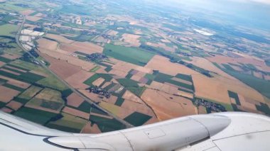 Bir uçak penceresinden görüldüğü gibi çeşitli tarlaların ve tarlaların manzaralı görüntüsü. Yeşiller, kahverengiler ve sarılar kırsal manzaraları sergiliyor, seyahat ve doğa fotoğrafçılığı temaları için ideal..