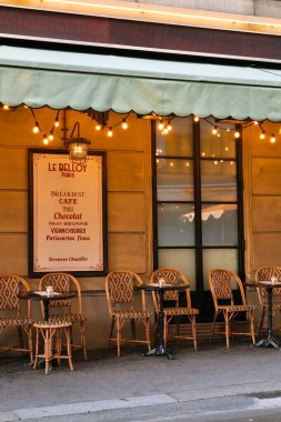 Paris, Polonya, 3 Ağustos 2025: Klasik açık hava oturma ve sıcak ışıklandırması olan pitoresk bir Paris kafesi. Sahnede güzel düzenlenmiş hasır sandalyeler, klasik bir menü tahtası ve sakin bir kahvaltıdan zevk almak için mükemmel bir ortam var.