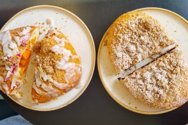 İçinde meyve dolgusu ve çeşitli malzemeler olan iki tabak. Bir hamur işi dilimlenmiş, krema ve kırıntıların altında canlı bir dolgu ortaya koyarken, diğeri şeker tozuyla parçalanmış bir yüzey sergiliyor..