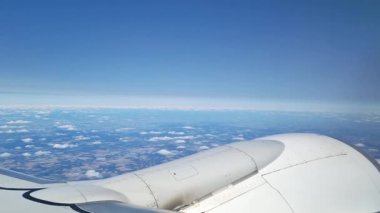 Manzaralı hava manzarası bir uçak penceresinden gözlemlenen geniş bir kara ve dağınık bulutları gösteriyor. Uçak kanadı, mavi gökyüzünün arka planına karşı seyahat ve keşiflerin vurgulanması için içerik sağlar..