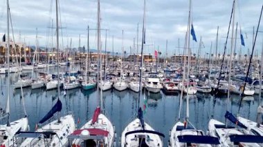 Barselona, İspanya, 25 Aralık 2024: Sakin bulutlu bir gökyüzü altında yelkenli ve yatlarla dolu hareketli bir marina. Direk ve su sanatı sıralarını yakalıyor. Denizcilik meraklıları için mükemmel sakin ama enerjik bir atmosferi yansıtıyor..