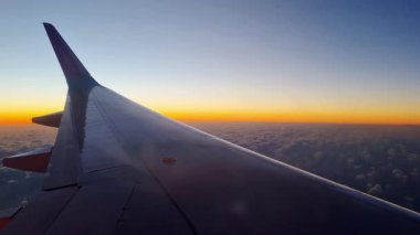 Barselona, İspanya, 4 Ocak 2025: Canlı bir günbatımı gökyüzü altında bir bulut denizi üzerinde uzanan uçak kanadı. Altın ufukta seyahat meraklıları ve havacılık tasvirleri için mükemmel yolculuk ve macera teması vurgulanıyor..