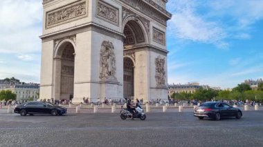 Paris, Fransa, 3 Ağustos 2025: Araçlar, arabalar ve bir motosiklet, açık mavi gökyüzünün altında Paris 'teki ikonik yay de triomphe' yi geçtiler. Tarihi anıt, canlı kent yaşamı ve mimarisini sergileyen yayalarla çevrilidir.