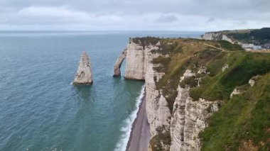Normandiya, Fransa 'daki etretat' ın ikonik tebeşir kayalıklarının manzarası, engin mavi okyanusun arka planına karşı çarpıcı kemer oluşumları içeriyor. Kısmen bulutlu gökyüzü derinlik katıyor, engebeli kıyı şeritlerini ve doğal güzellikleri vurguluyor.