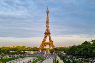 Paris, Fransa, 3 Ağustos 2025: Eyfel Kulesi Paris 'te alacakaranlık gökyüzüne karşı görkemli bir şekilde duruyor, yemyeşil bahçeler ve kalabalık kalabalıklarla çevrili. Mimari güzelliğin ve hayat dolu şehir hayatının bu ikonik simgesi, dünya çapında turistlerin ilgisini çekiyor..