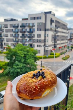 Üstü çikolata parçacıkları ve beyaz bir tabakta kırıntılarla kaplı nefis bir hamur işi, çağdaş şehir dairelerinin arka planına dayanır. Sahne mutfak zevkini şehir yaşam tarzıyla harmanlıyor, sabah keyfi sergiliyor..