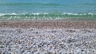 Sahile çakıl taşlarıyla kaplı ve dalgaların usulca kıyıya vurduğu sakin bir sahil manzarası. berrak mavi su, pürüzsüz, yuvarlak taşlarla çok güzel zıtlaşır ve plaj temalı doğal bir kompozisyon oluşturur.