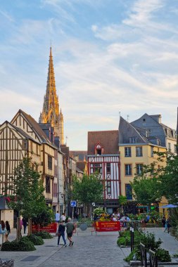 Rouen, Fransa, 28 Temmuz 2025: Canlı yarı ahşap evleri ve yüksek bir kilise kulesi olan Avrupa caddesi manzarası. Sahnede yemyeşil ve yayalar güzel boyanmış gökyüzünün altında sıcak bir akşamın tadını çıkarıyorlar..