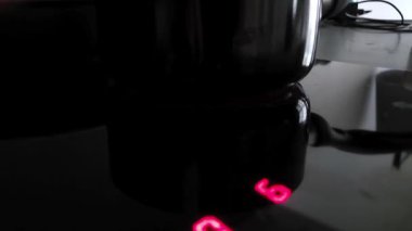 Kırmızı sayısal göstergeler gösteren parlak bir indüksiyon sobası modern mutfak ortamını yansıtır. Gelişmiş teknolojiyi vurgulayan bu sahne, dijital kontrolleri olan, çağdaş tasarım ve işlevselliği vurgulayan siyah, parlak bir yüzeye sahiptir..