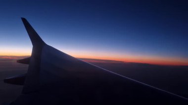 Barselona, İspanya, 4 Ocak 2025: Gün batımı renkleri uçak penceresinden gökyüzünü aydınlatarak, uçuşta seyahat etmenin huzurlu güzelliğini yansıtır. Kanat silueti, alacakaranlık renklerine derinlik katar..