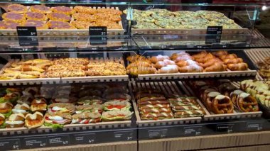 Viyana, Avusturya, 5 Mayıs 2025: Pizzalar, pastalar ve sandviçler de dahil olmak üzere çeşitli hamur işleri iyi aydınlatılmış bir fırın vitrininde düzenleniyor. Etiketler fiyatlandırmayı ve seçenekleri göstermekte, taze, lezzetli müşteriler için lezzetli bir seçim sunmaktadır