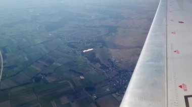 Hava perspektifi, yamalı tarlaları ve küçük kasabaları olan pitoresk bir kırsal alanı gösteriyor. Uçak kanadı dinamik bir element ekler, aşağıdaki kırsal alanların dingin genişliği.