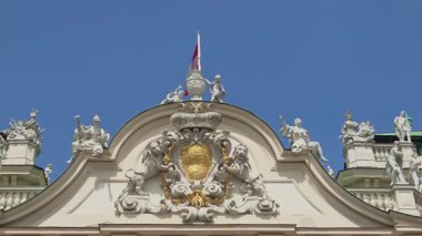 Viyana, Avusturya, 3 Mayıs 2025: Barok mimari detayları, açık mavi gökyüzüne karşı karmaşık heykeller ve dekoratif tasarımlar içeren tarihi bir Avrupa binasını süslüyor. Bayrak, klasik ve zarif yapıya ulusal gurur katar..