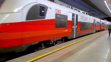 Viyana, Avusturya, 3 Mayıs 2025: Şık bir şehir treni çağdaş bir yeraltı istasyonundan hızla geçiyor, kentsel yaşamı ve modern ulaşımı yakalıyor. Canlı kırmızı dış görünüm istasyonlara karşı duruyor sessiz tonlar, banliyö beklerken