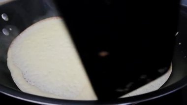 A moment in the pancake-making process, showcasing a pancake being flipped in a skillet with a spatula. the texture and color of the pancake contrast against the black skillet, the cooking technique.
