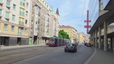 Vienna, Austria, May 3, 2025: A vibrant urban cityscape featuring a tram and cars navigating a lively street, flanked by residential and commercial buildings under a clear blue sky. the scene reflects everyday urban transportation and architecture.