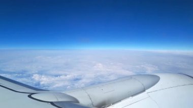 Scenic aerial view from an airplane window showing a vast cloudscape beneath a bright blue sky. the image highlights the wingtip of the aircraft, capturing the essence of air travel and the serene beauty above the clouds.