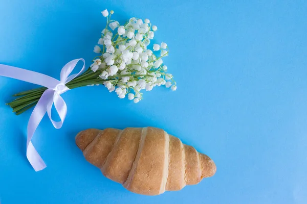 Mavi arka planda Fransız kruvasanı ve vadideki zambak. Kahvaltı.