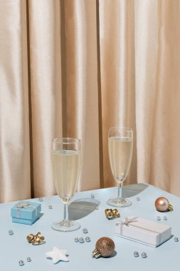 Şampanya bardakları, parlak Noel mücevherleri, hediyeler ve ipeksi saten perdeler ile yaratıcı bir düzenleme. Yeni yıl partisi geçmişi, çağdaş estetik tatil düzeni.
