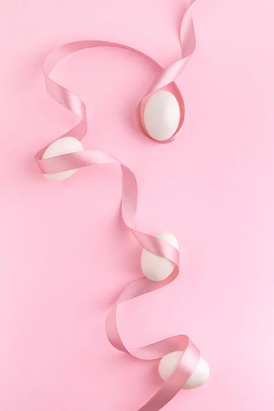 ピンクの背景に白い卵と巻きサテンリボンで最小限のイースターの芸術的な組成 春休み審美的なフラットレイアウト ストック写真