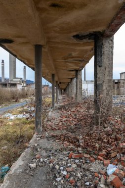 Corridor of an old chemical factory looted dilapidated crumbling bricks gravel concrete. Remains of an abandoned chemical industry factory in shambles. Run down walls in disrepair. Disaster ruins. Cloudy skies and concrete