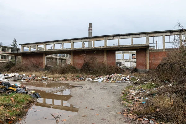 Remains of an old chemical factory looted dilapidated crumbling puddle water. Remains of an abandoned chemical industry factory in shambles. Run down walls in disrepair. Disaster ruins. Cloudy skies and concrete