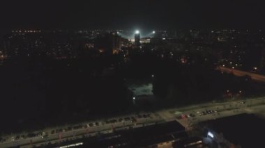 Gece lambası arabalarıyla bir kasabanın üzerinden uçmak. Hava aracı atışı. Kara gökyüzü. Konut binaları sporu. İnsansız hava aracı sokakları