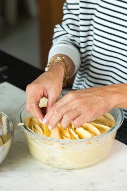 Woman putting apples while cooking apple pie in the modern kitchen