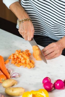 Woman slicing vegetables while cooking stew. Close up of woman hands cutting vegetables on a cutting board at the modern kitchen