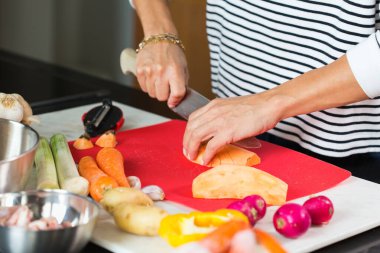 Woman slicing vegetables while cooking stew. Close up of woman hands cutting vegetables on a cutting board at the modern kitchen