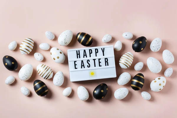 Happy Easter frame with golden, white, black dotted and striped eggs on a pink background. Top view, flat lay. Modern Easter greeting card